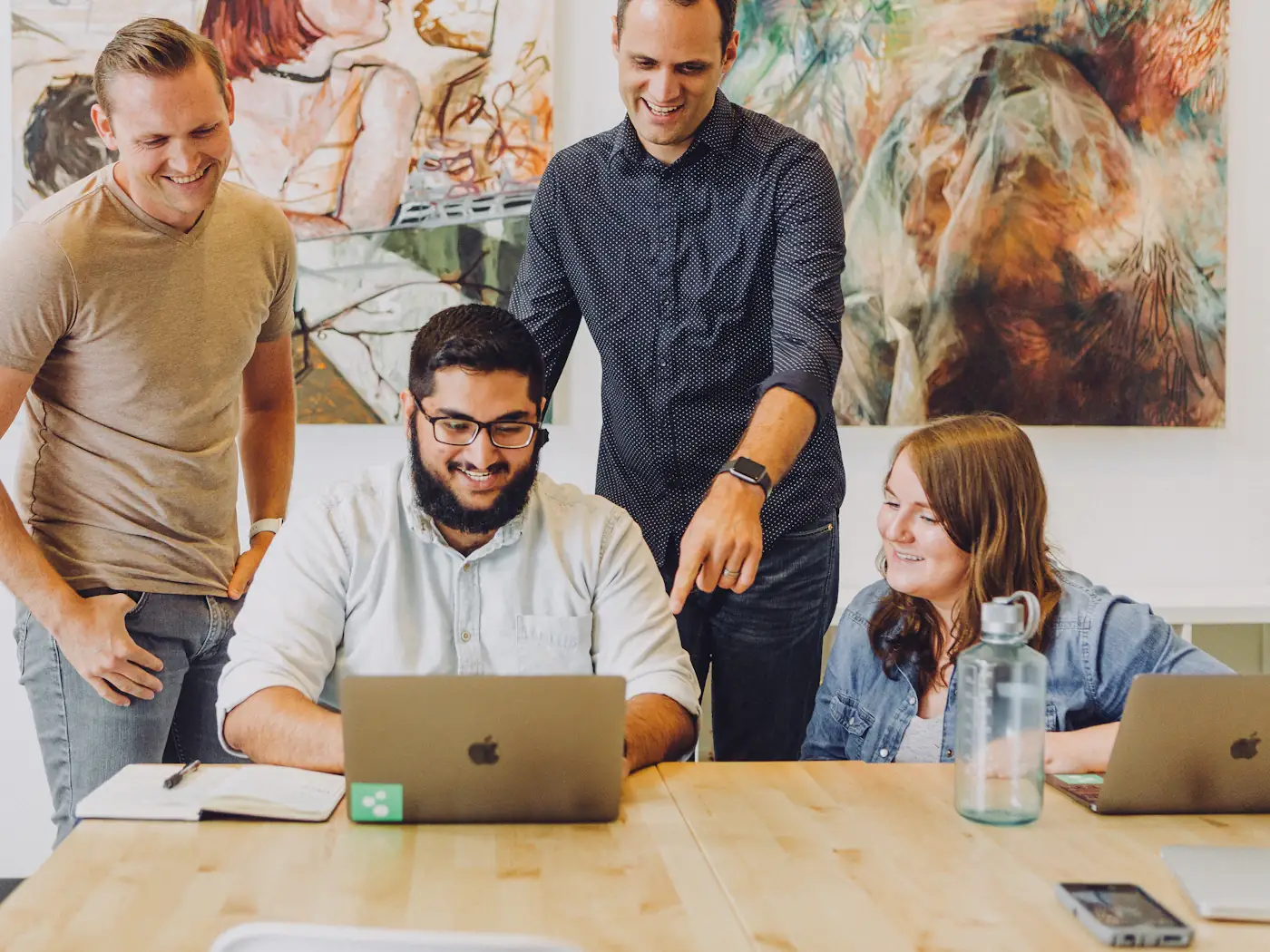 Four coworkers smiling around a laptop as one points out a detail on the screen