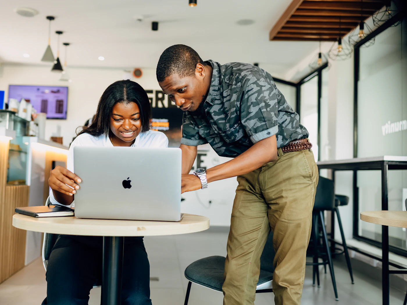 Two people at a cafe table, smiling as they look over a laptop together