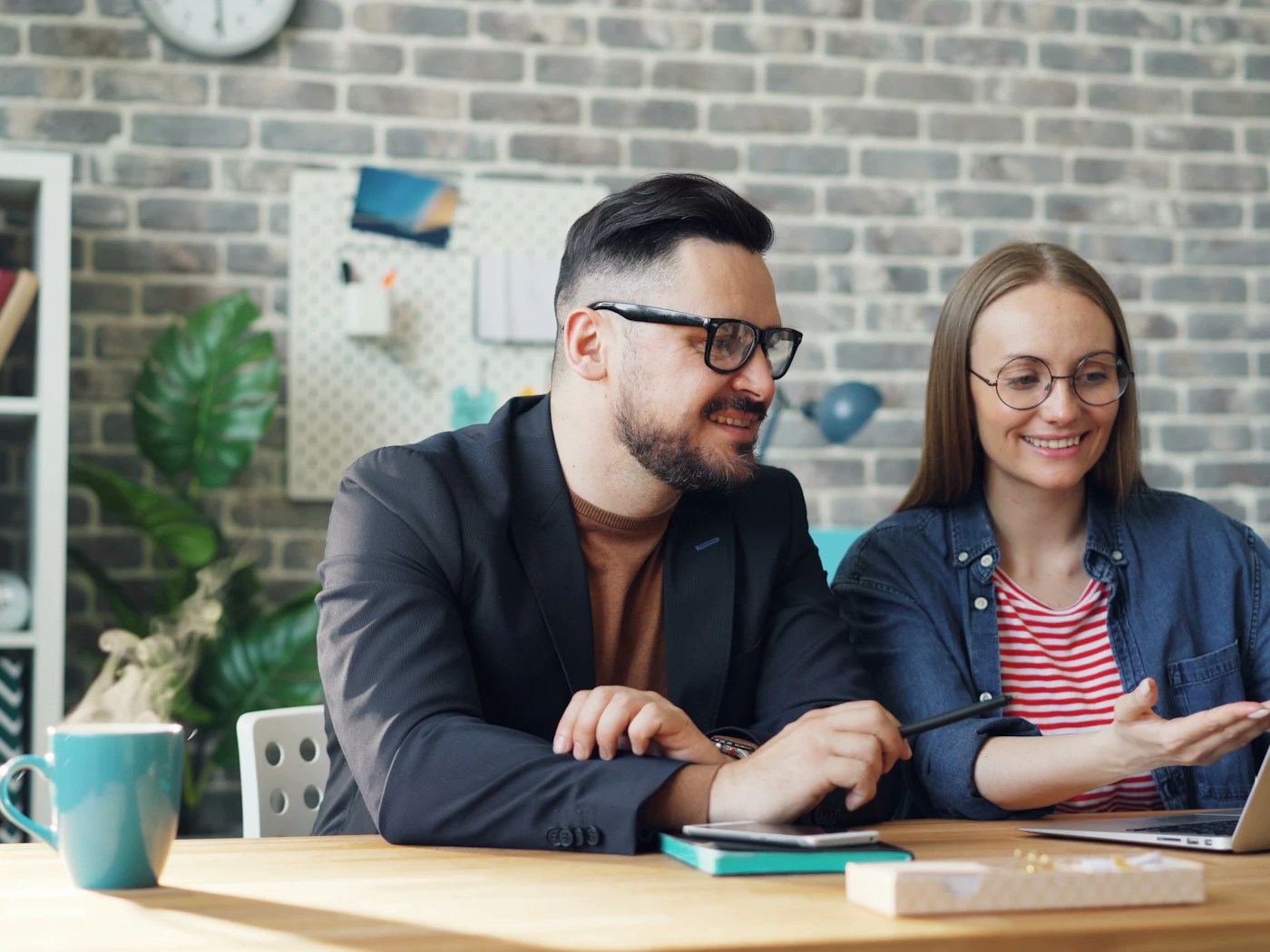 Two colleagues smiling as they work through a plan together at a laptop